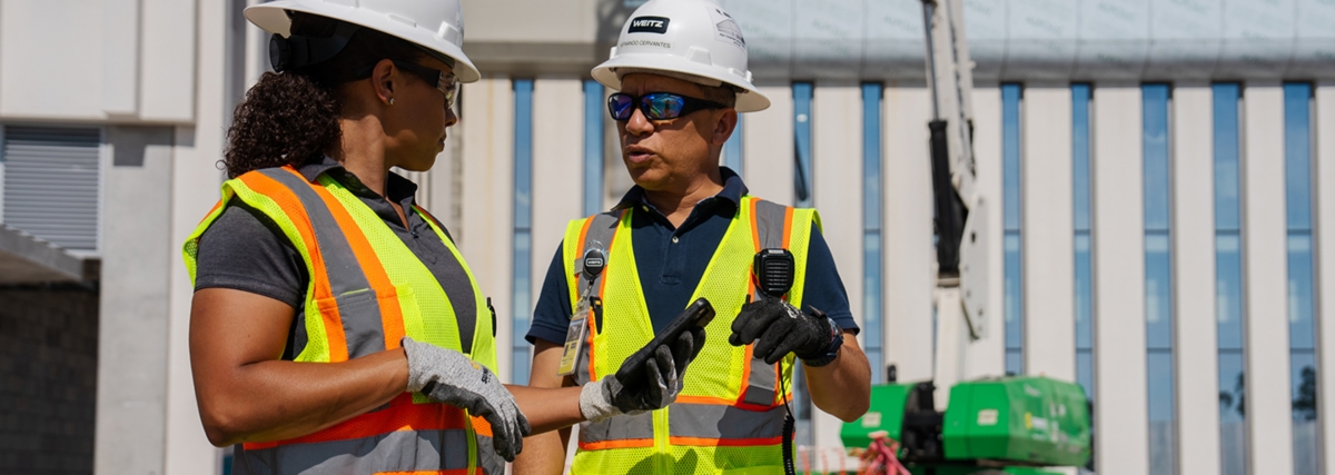 Two people wearing yellow safety vests and hard hats at a construction site.