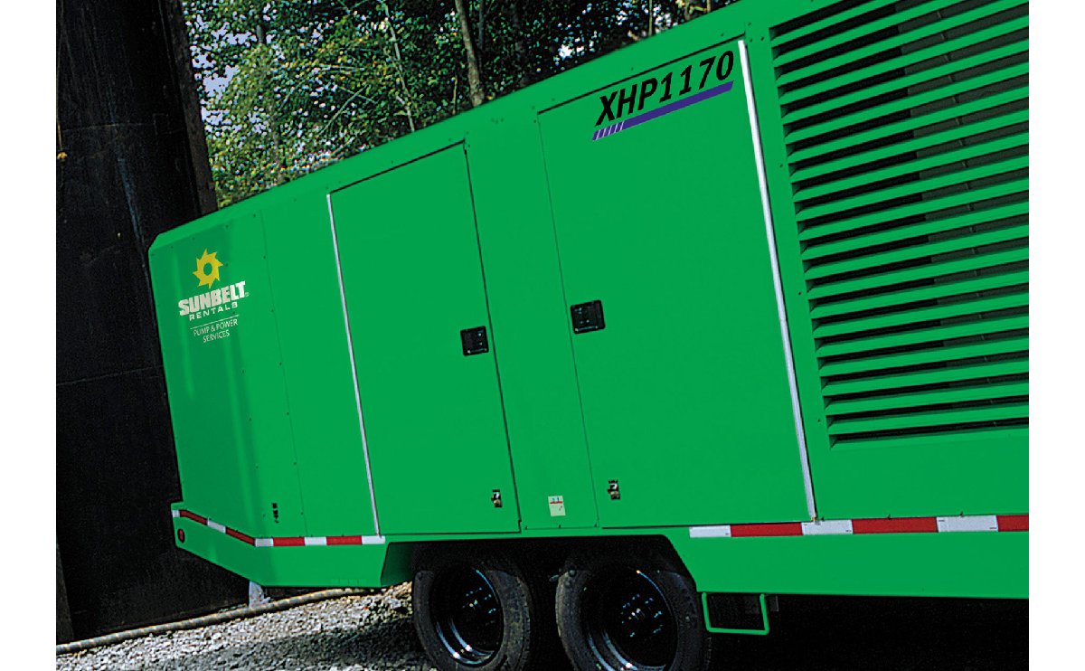 A green Sunbelt Rentals air compressor parked on a gravel pad.