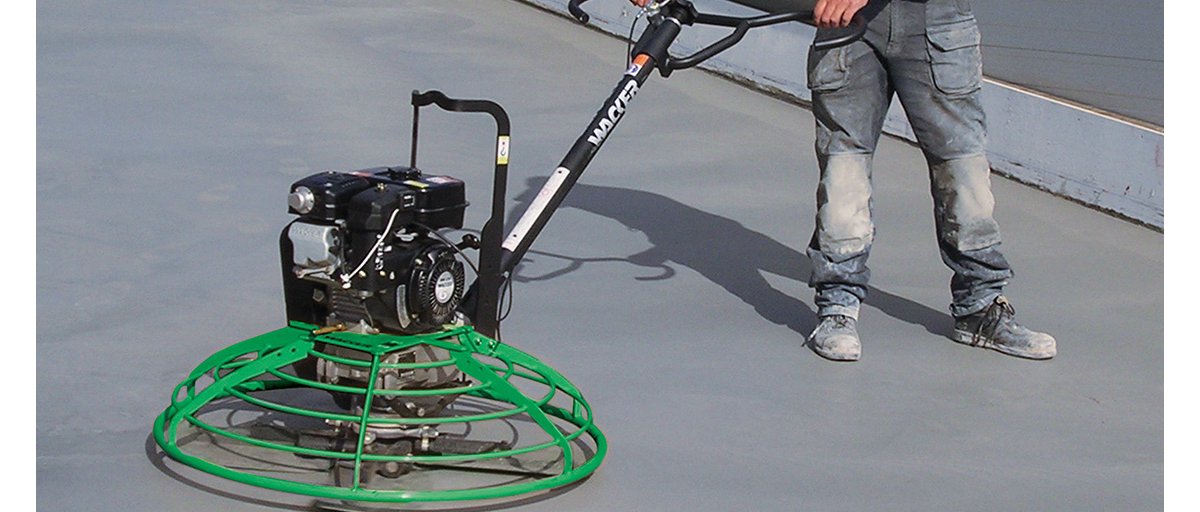 A construction worker uses a gas-powered walk-behind concrete power trowel to smooth concrete.