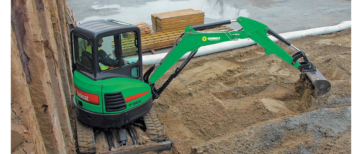 A person scoops dirt with a green Sunbelt  Rentals excavator.