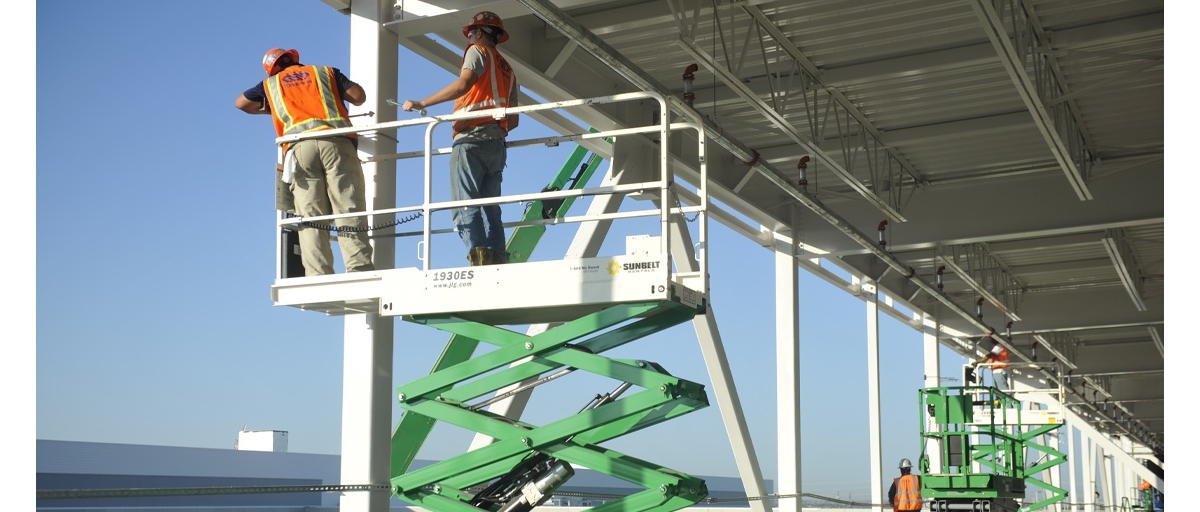 Construction workers use scissor lifts to install things on a metal building.