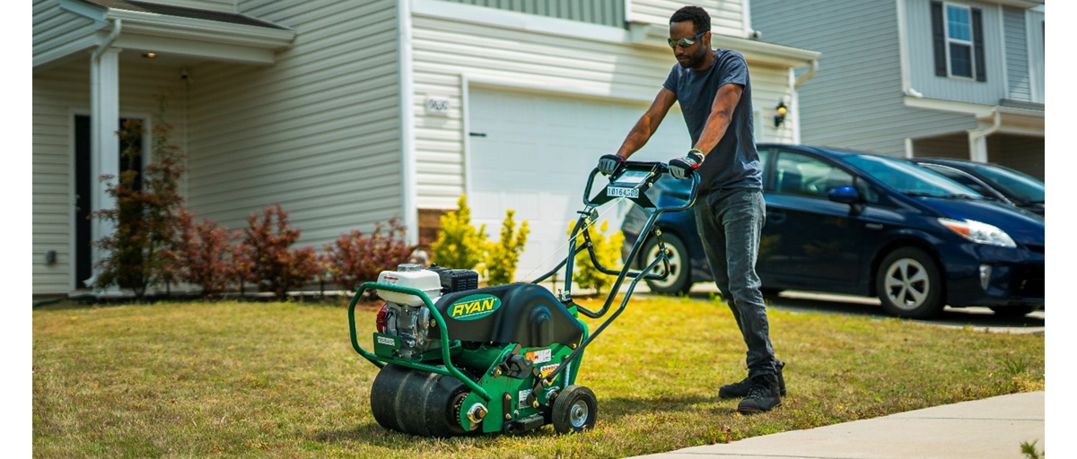 Man aerating lawn in front of a house