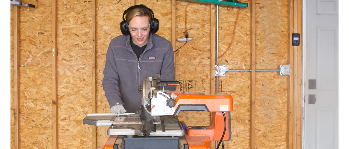 Person wearing safety glasses and ear muffs using an electric tile saw.