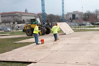 Two people wearing bright green shirts laying ground protection mats over grass.