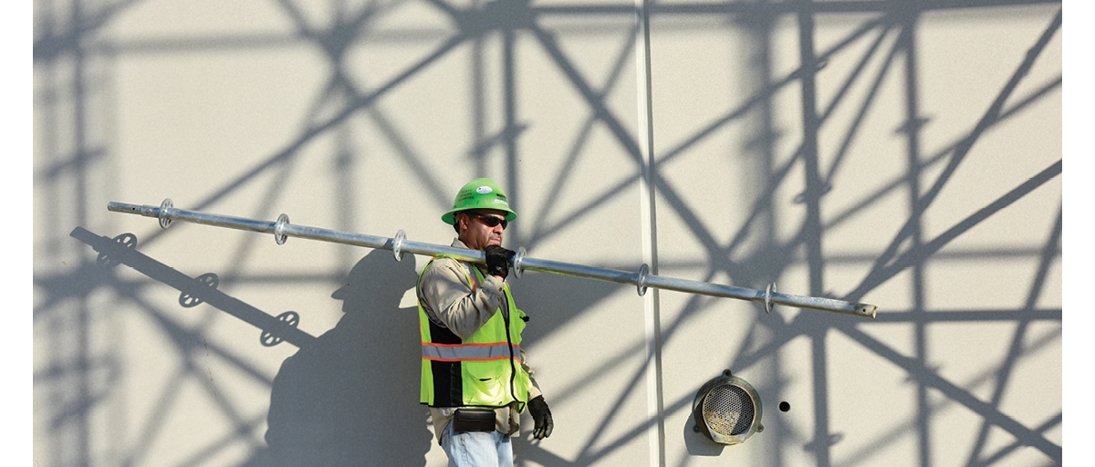 Construction worker walking with scaffolding equipment.