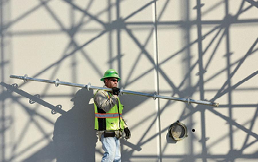 Construction worker walking with scaffolding equipment.