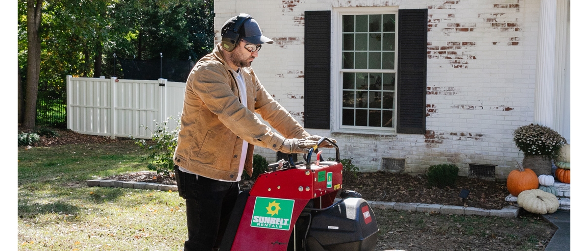 Person in a yard using a ride on aerator from Sunbelt Rentals.