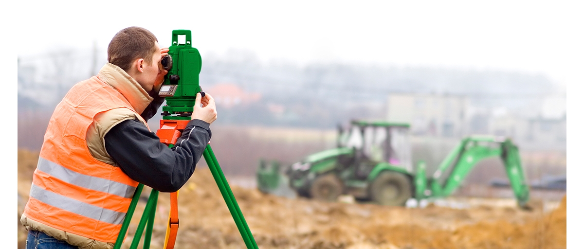 A man wearing an orange safety vest looks through a laser level on a jobsite where Sunbelt Rentals equipment is being used.