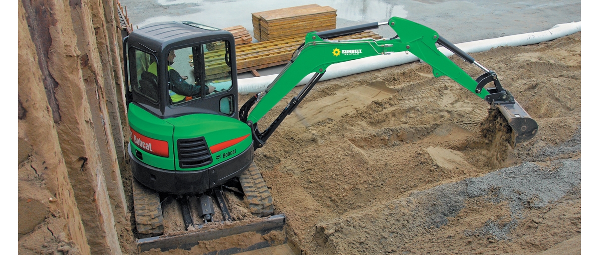 A construction worker scoops dirt with an excavator from Sunbelt Rentals.