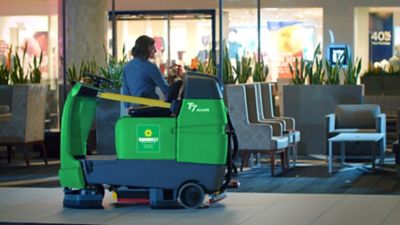 Someone driving a ride-on floor scrubber from Sunbelt Rentals.