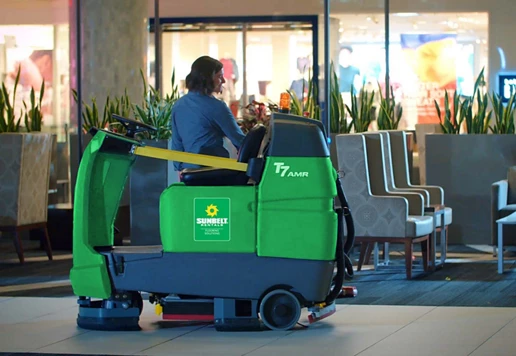 Someone driving a ride-on floor scrubber from Sunbelt Rentals.