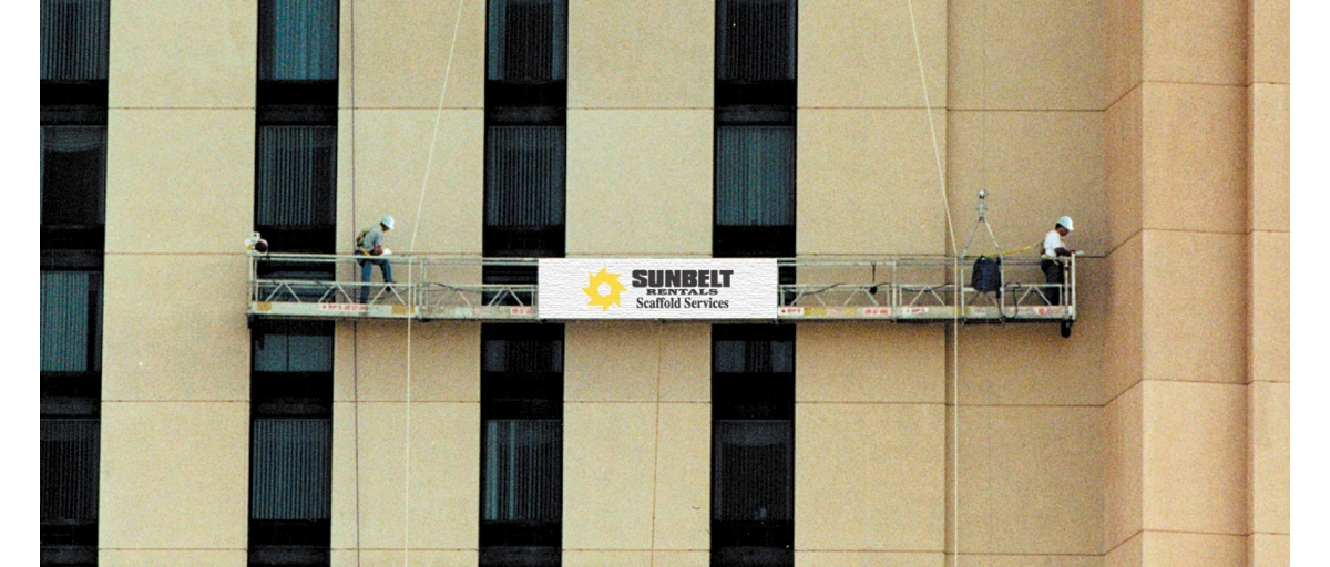 People standing on a swing stage from Sunbelt Rentals Scaffold Services, attached to the side of a tall building.