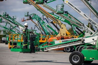 Someone wearing safety apparel on a manlift, surrounded by other manlifts in a lot.
