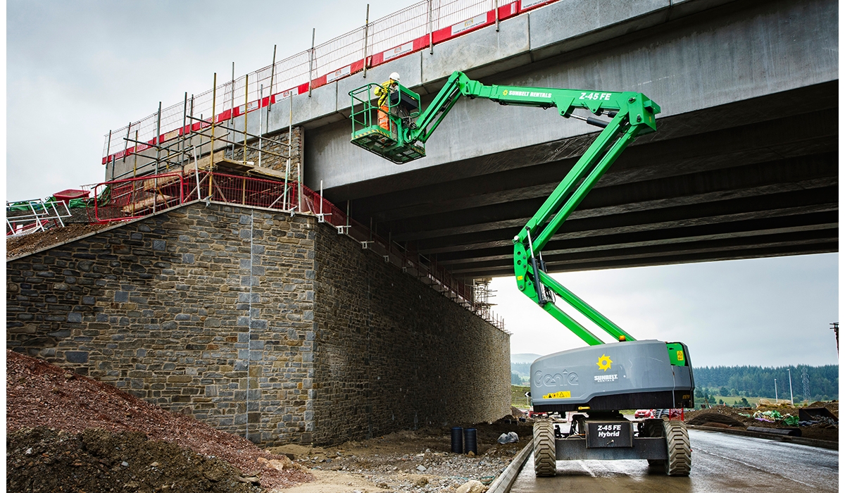 Someone operates an articulated boom lift alongside a bridge.