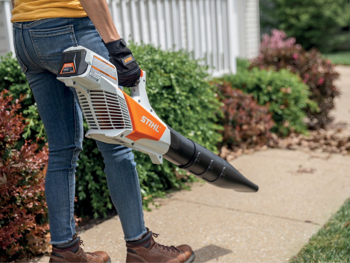 A handheld blower used to blow leaves on a sidewalk.