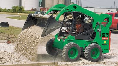 A skid steer loader dumping gravel at a job site.