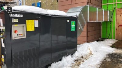 A direct-fired heater installed outside of a building, surrounded by snow.