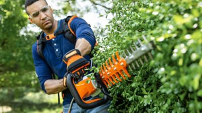 Someone operating a cordless hedge trimmer to maintain shrubs.