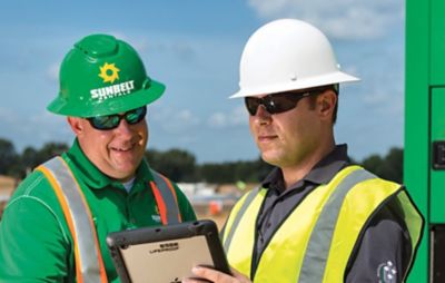 Two people wearing safety equipment looking at a tablet device.