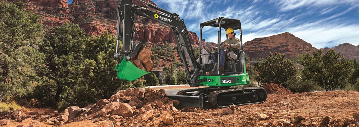 Someone operating an excavator from Sunbelt Rentals, picking up rocks at a mountainous job site.