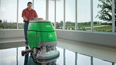 Someone cleaning a building's floor with a walk-behind floor scrubber.