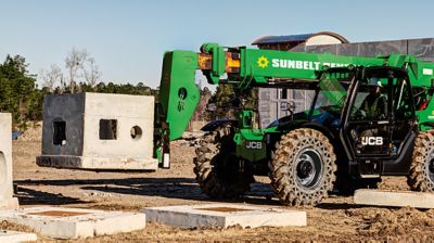 Someone operating a forklift to raise a small concrete structure off the ground.