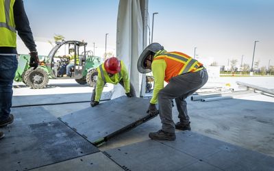 Two people wearing safety apparel installing ground protection matting.