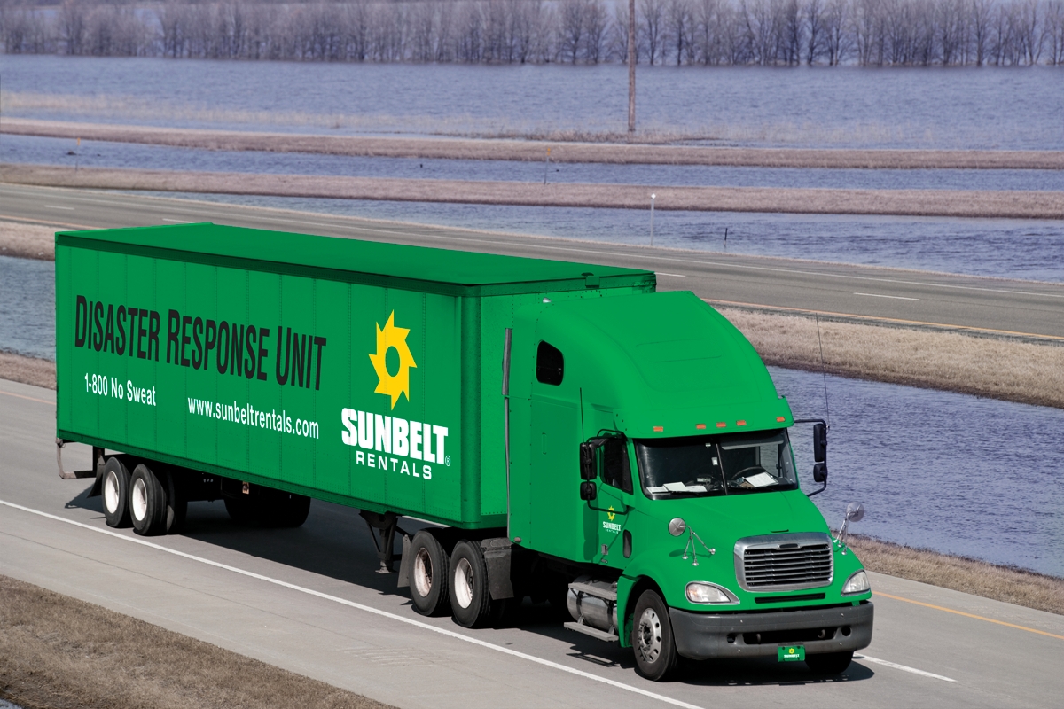 A Sunbelt Rentals Disaster Response Unit truck driving down a road alongside water.