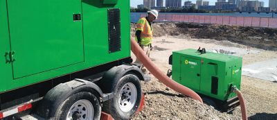 Someone wearing safety apparel stands with pump equipment at a jobsite.