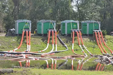 Pumps from Sunbelt Rentals removing water via long orange hoses in a grassy field.