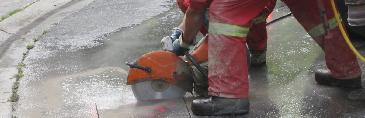 Worker cutting asphalt with a concrete saw.