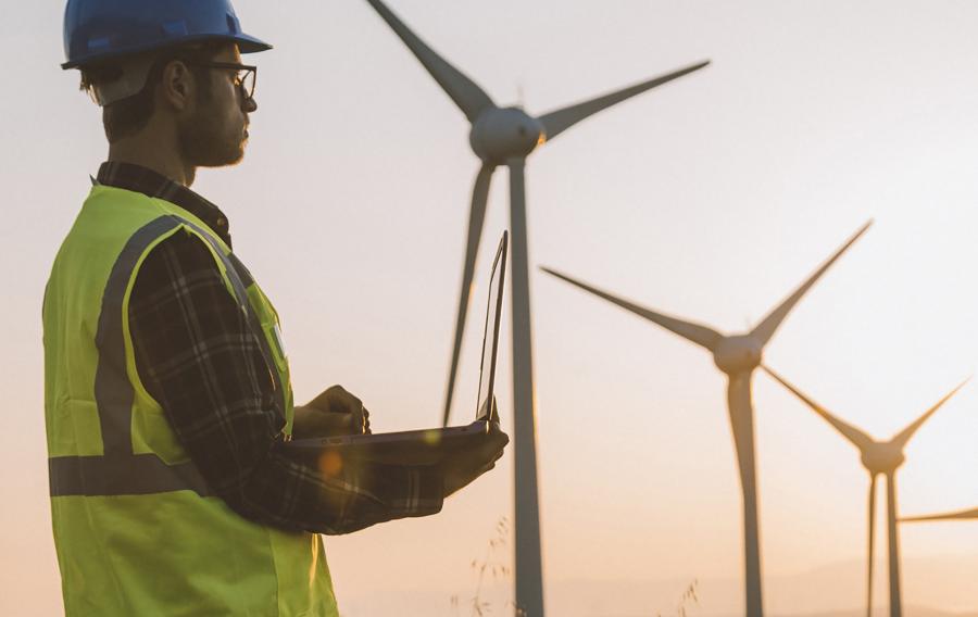 Someone wearing safety apparel standing in front of wind turbines.