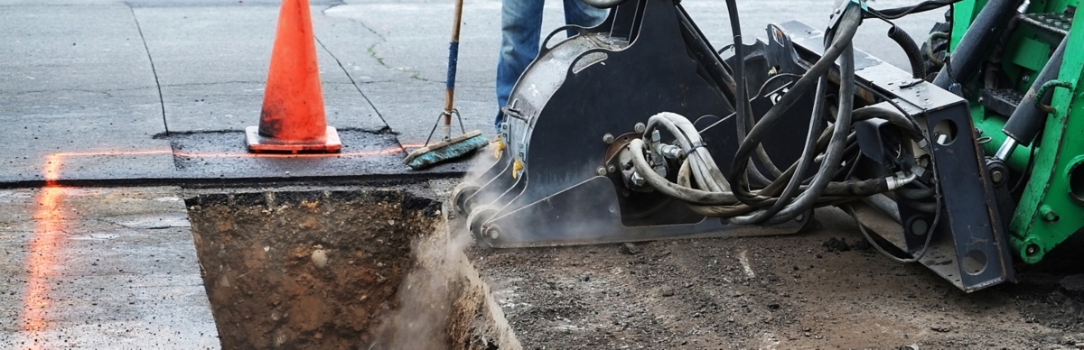 Open utility trench across city street while crew working on a rainy day.