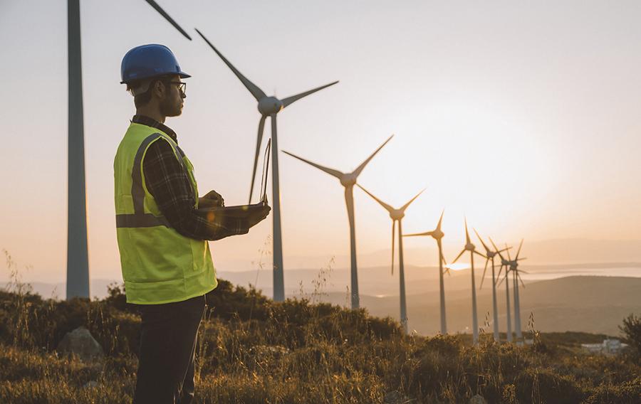 Someone wearing safety apparel standing in front of wind turbines.