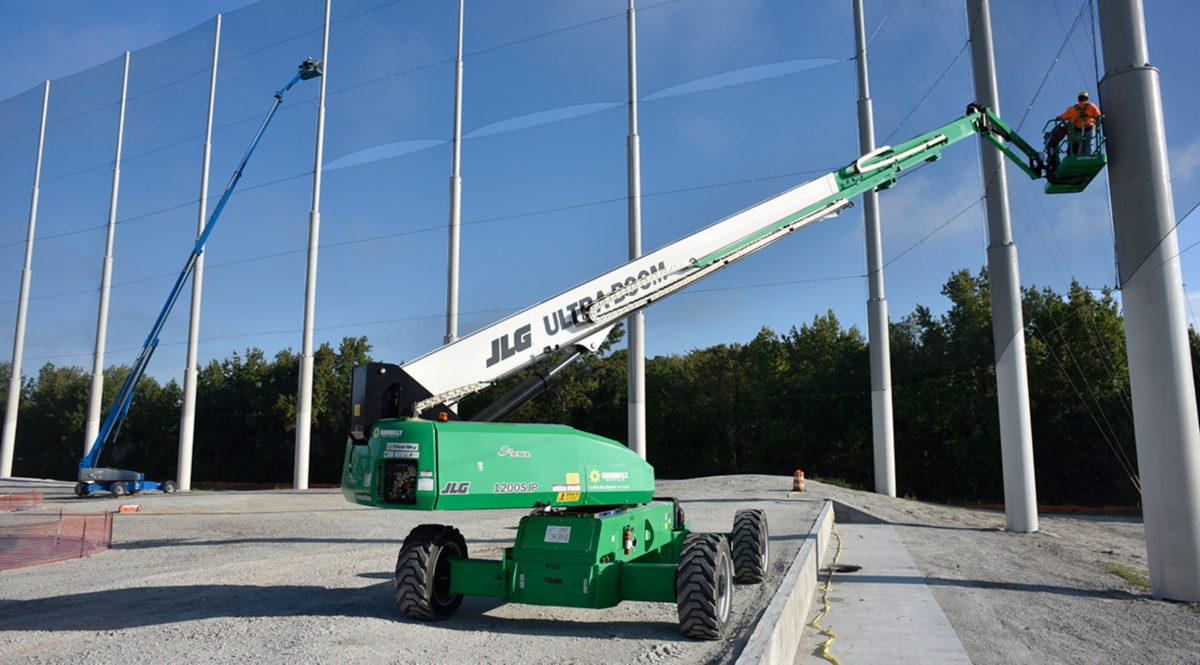 Boom lifts in operation at a job site with poles and netting.