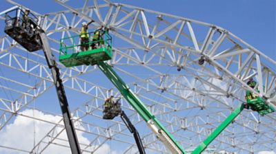 Boom lifts being used to work on a tall, metal-framed structure.