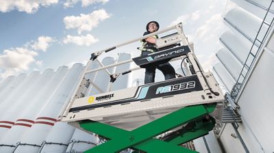 Someone using a mobile elevated work platform from Sunbelt Rentals outside an industrial facility.