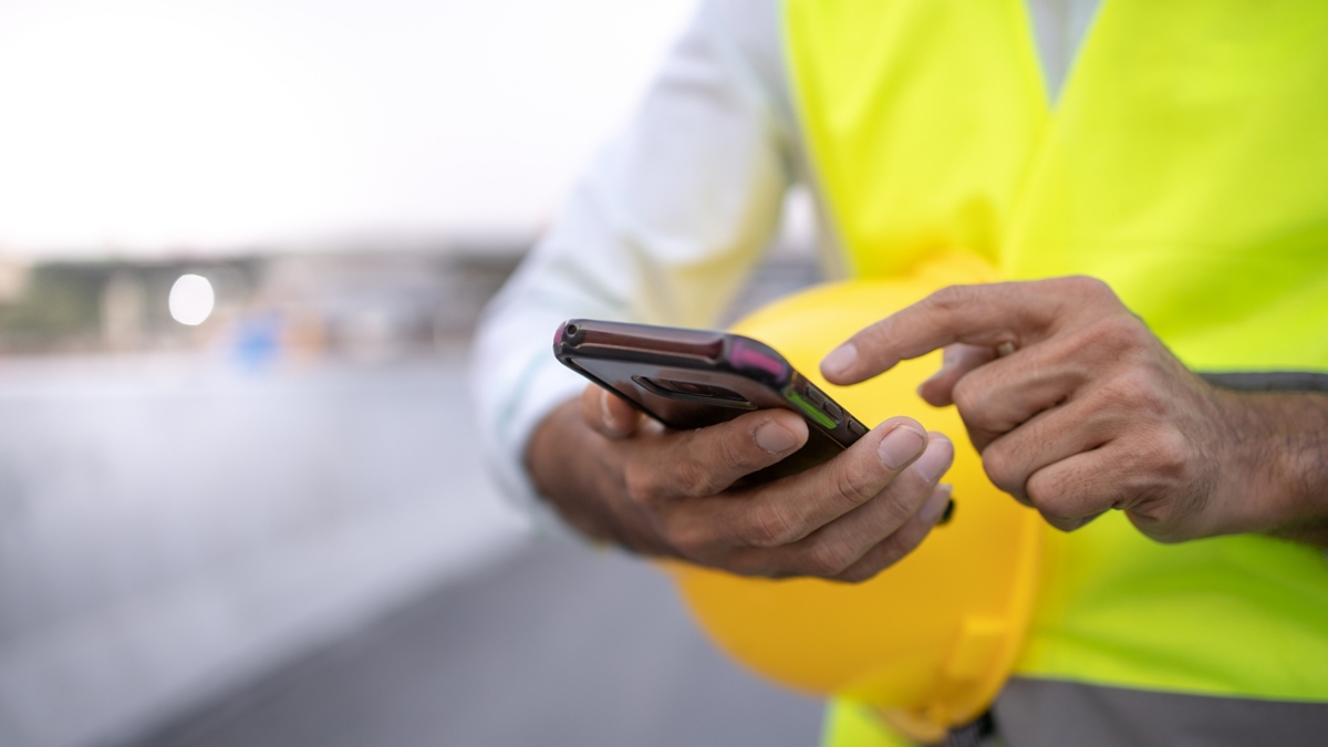 A person wearing a safety vest uses a mobile phone.