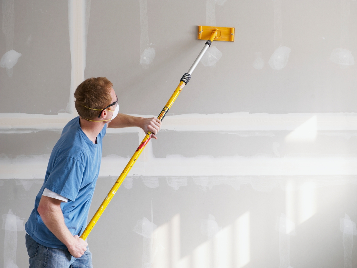 Someone sanding drywall with a long pole sander.