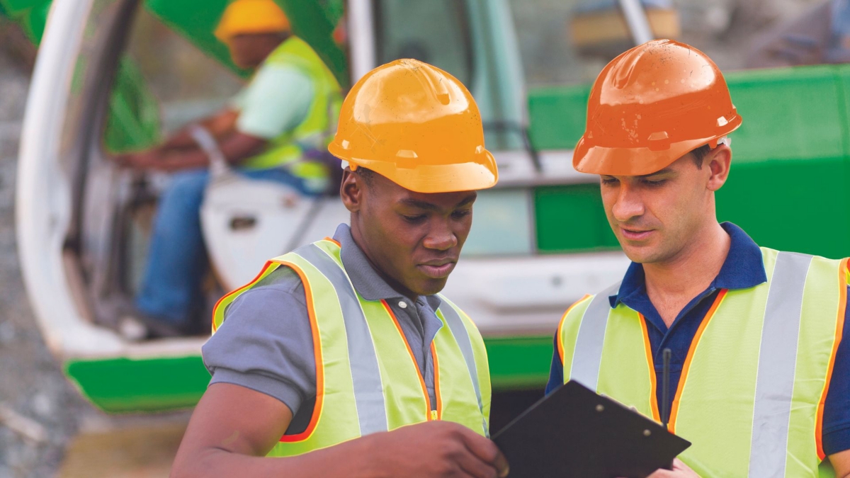 Two people wearing safety apparel at a construction site looking at tablet device.