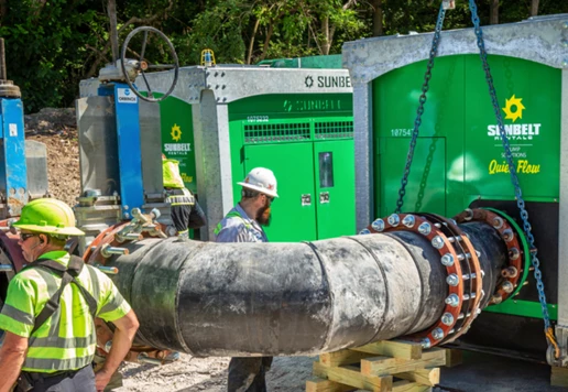 Two workers wearing safety apparel walking around a job site with Quiet Flow pumps from Sunbelt Rentals.