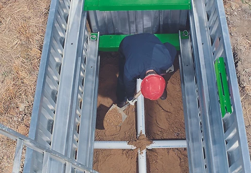 Someone wearing a helmet standing inside of a trench box, shoveling dirt.