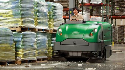 Someone driving a ride-on floor sweeper in a warehouse.