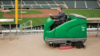 Someone driving a ride-on mid-frame micro scrubber at a stadium.