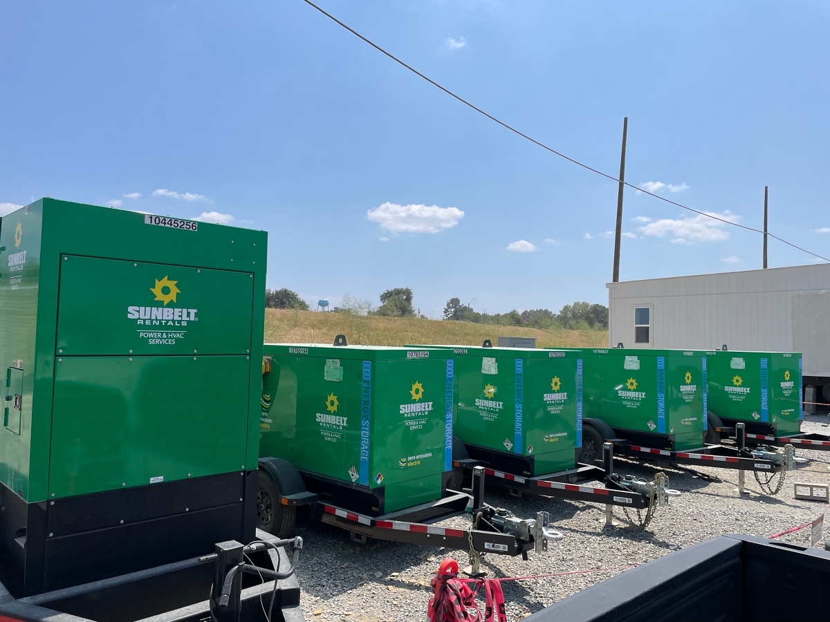 A row of green Sunbelt Rentals generators is parked outdoors on trailers in a gravel lot.
