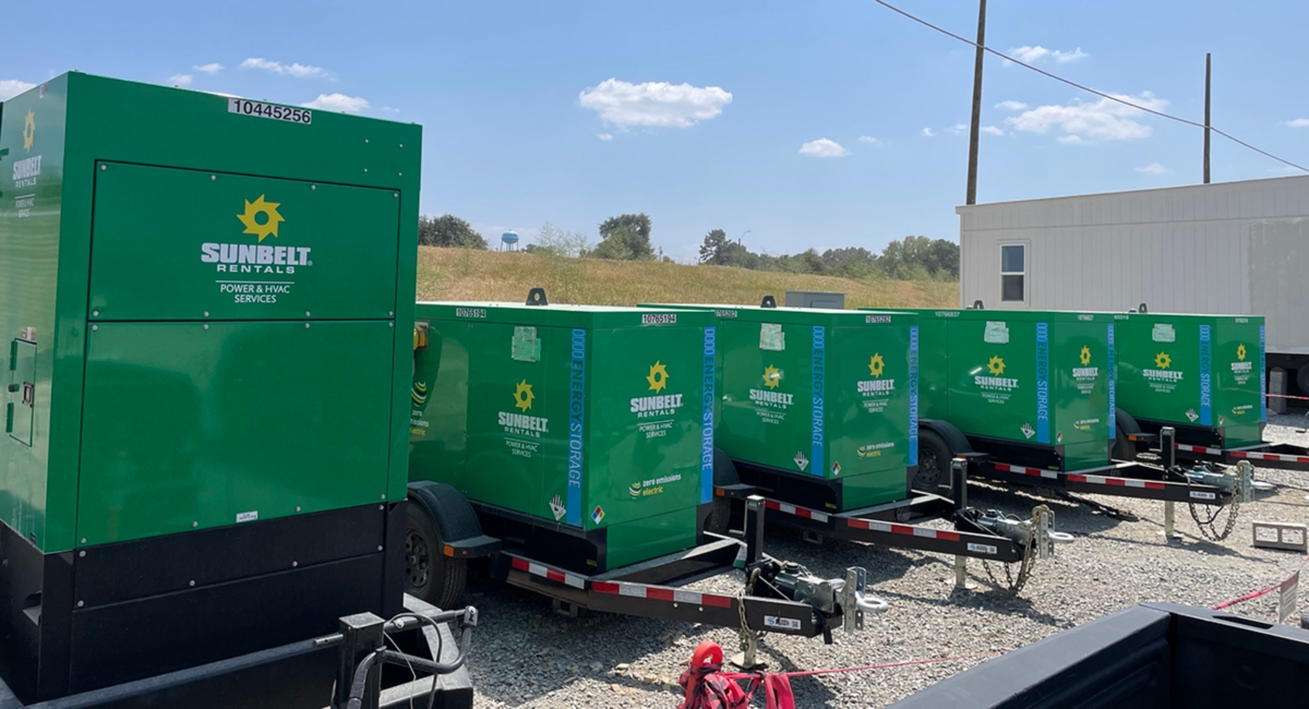 A row of Sunbelt Rentals battery energy storage systems parked in a gravel lot.