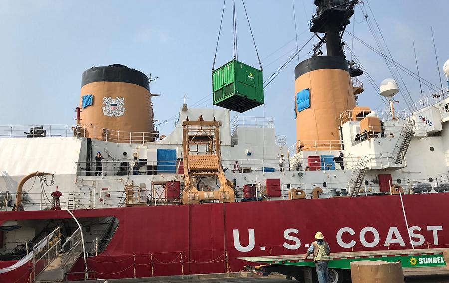 A U.S. Coast Guard ship docked at a port while a Sunbelt Rentals loading bank is lifted onto the ship. 