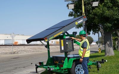 Someone wearing safety apparel standing with a solar light tower.