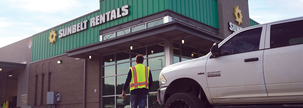 Someone wearing a safety vest walking up to a Sunbelt Rentals storefront.