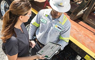 A man and woman reviewing a tablet computer on a construction site.